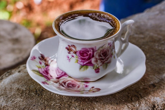 Elegant hand-painted teacup and plate holding steaming black tea.